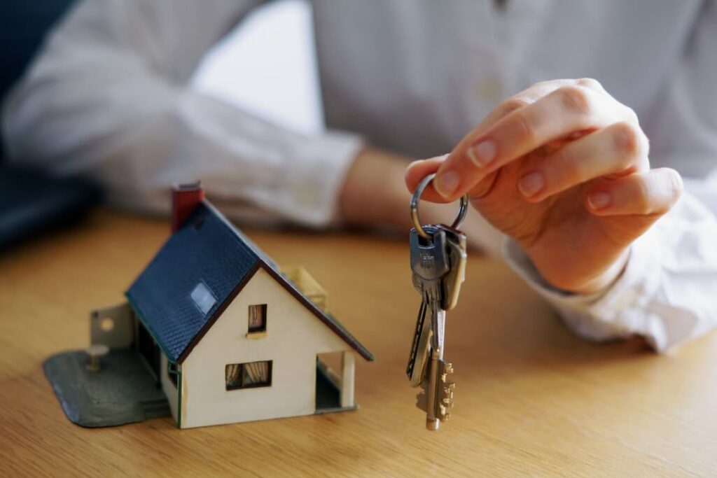hombre sosteniendo llaves y casa de madera de fondo