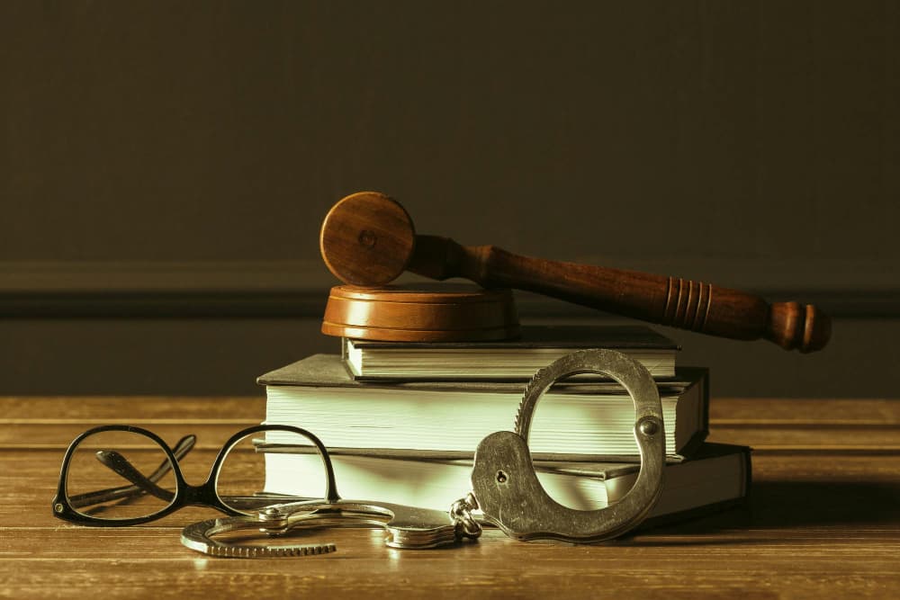 Libros jurídicos con mazo, gafas y esposas sobre mesa, concepto de delito penal